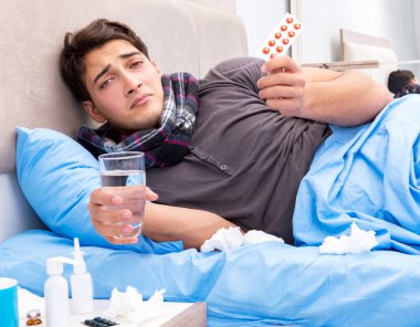 Grip olmuş hasta adam yatakta yatıyor.