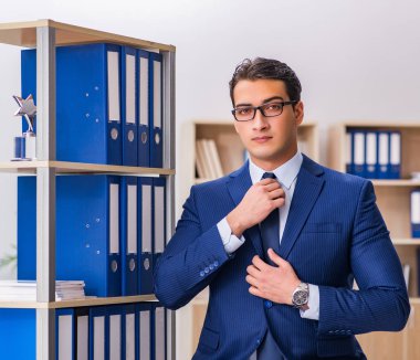 Dosyalarla rafın yanında duran genç adam.