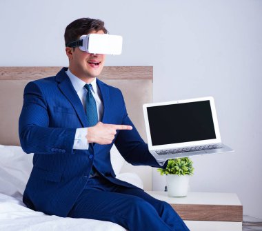Yatak odasında sanal gerçeklik kulaklığı takan bir iş adamı.