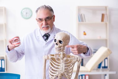 İskeleti olan yaşlı erkek doktor.