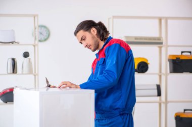 Genç müteahhit atölyede buzdolabını tamir ediyor.