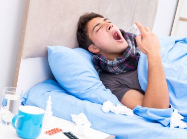 Grip olmuş hasta adam yatakta yatıyor.