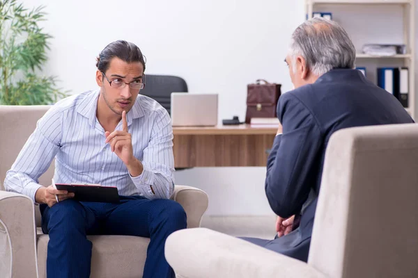 Homem velho visitando jovem médico psicólogo masculino — Fotografia de Stock