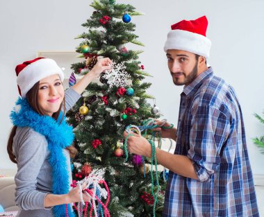 Genç aile Noel ağacını mutlu bir vesileyle süslüyor.