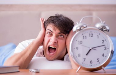 Yataktaki adam alarm yüzünden uykusuzluk çekiyor.