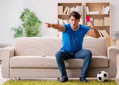Evdeki kanepede oturup futbol izleyen bir adam.