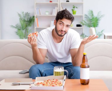Pizza yiyen adam evde yemek yiyor, dinleniyor.