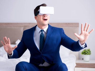 Yatak odasında sanal gerçeklik kulaklığı takan bir iş adamı.