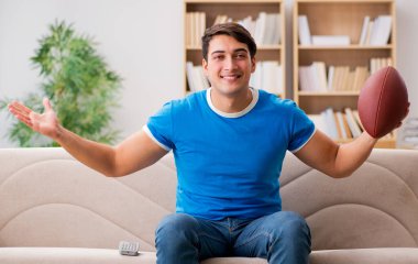 Evdeki kanepede oturup futbol izleyen bir adam.