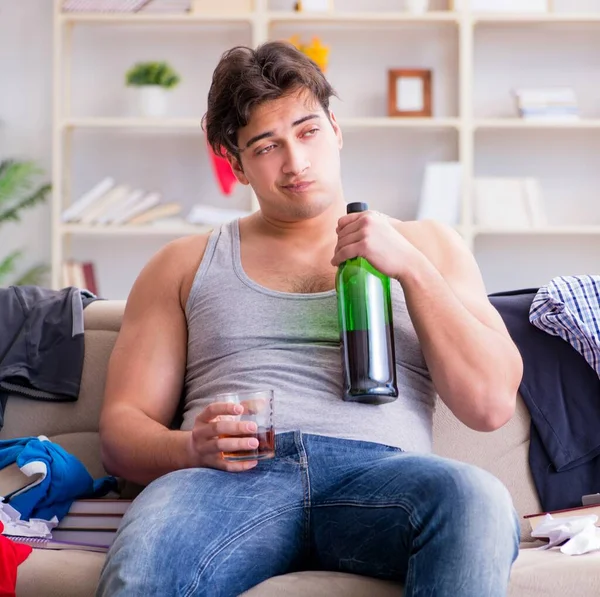 Ung man student berusad dricka alkohol i ett rörigt rum — Stockfoto