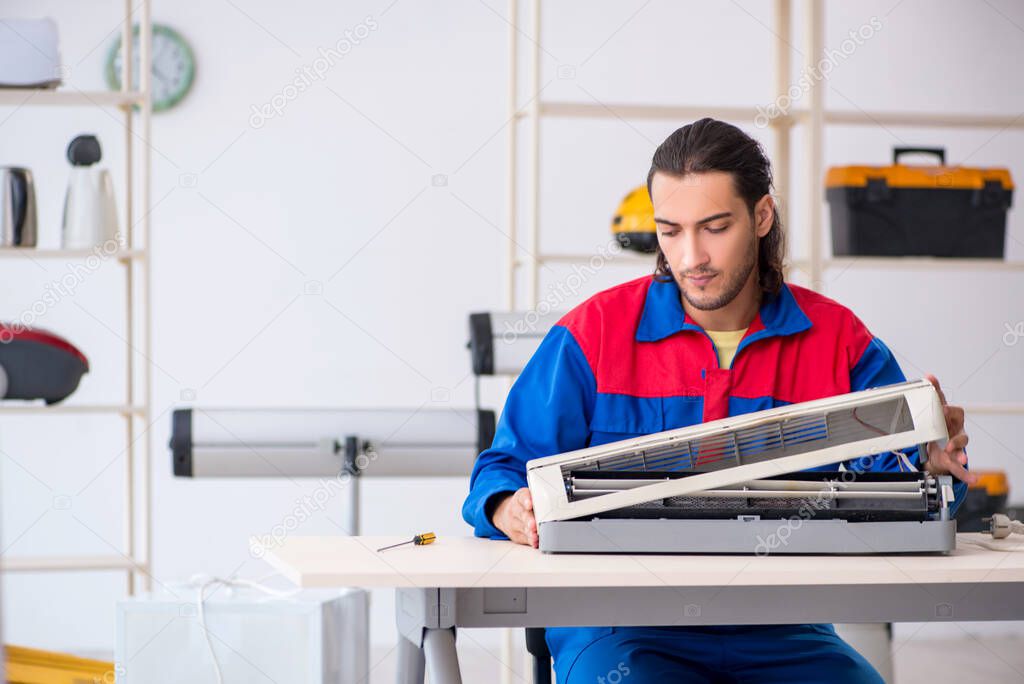 Young male contractor repairing air-conditioner at workshop