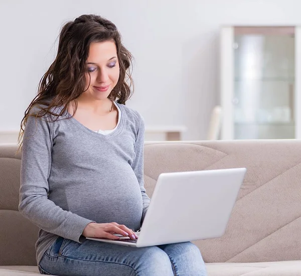 Donna incinta che lavora su laptop seduta sul divano — Foto Stock