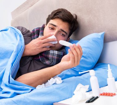 Grip olmuş hasta adam yatakta yatıyor.