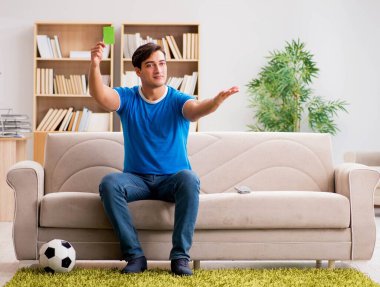 Evdeki kanepede oturup futbol izleyen bir adam.