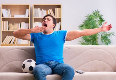 Evdeki kanepede oturup futbol izleyen bir adam.