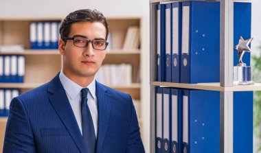 Dosyalarla rafın yanında duran genç adam.