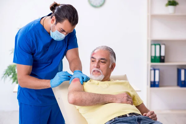 Verwondde oude man op bezoek bij jonge mannelijke arts traumatoloog — Stockfoto