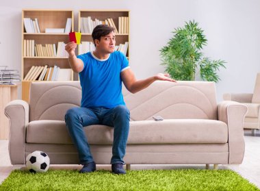 Evdeki kanepede oturup futbol izleyen bir adam.