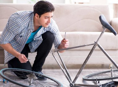 Evde bisiklet tamir eden genç bir adam.