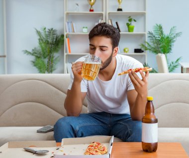 Pizza yiyen adam evde yemek yiyor, dinleniyor.