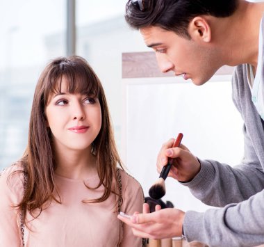 Güzellik salonunda güzel bir kadın için makyaj yapan adam.