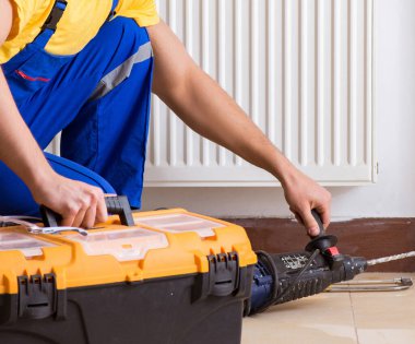 Genç tamirci müteahhit ısıtma panelini tamir ediyor.