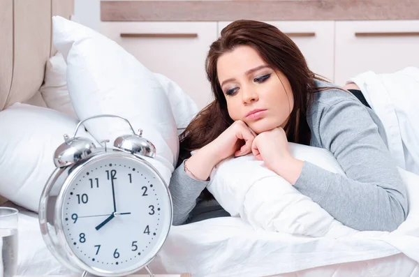 Mujer joven acostada en la cama en concepto de gestión del tiempo —  Fotos de Stock