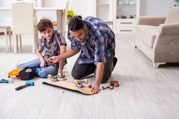 Giovane padre che ripara skateboard con suo figlio a casa — Foto Stock