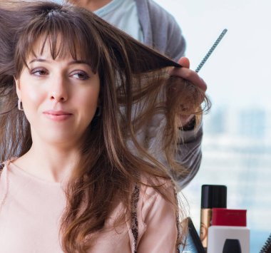 Erkek stilisti bir kadınla güzellik salonunda çalışıyor.