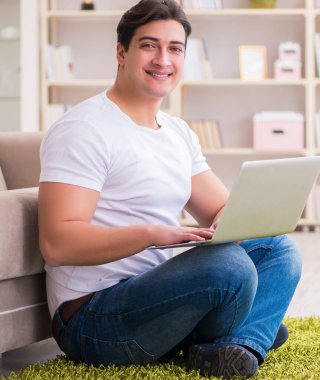 Evde, halı döşemesinde dizüstü bilgisayarda çalışan bir adam.