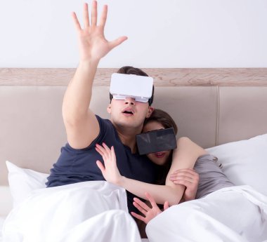Yatakta sanal gerçeklik gözlüklü eş ve koca.