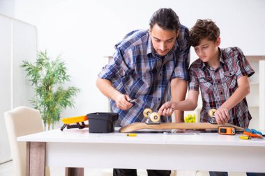 Genç baba oğluyla kaykay tamir ediyor.