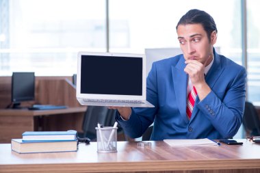 Genç yakışıklı işadamı ofiste oturuyor.