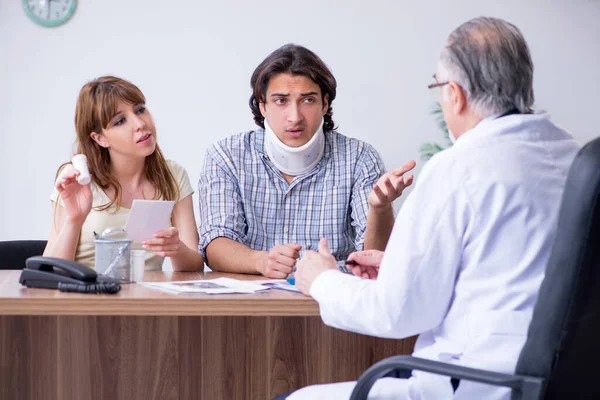 Pareja joven visitando viejo médico masculino — Foto de Stock