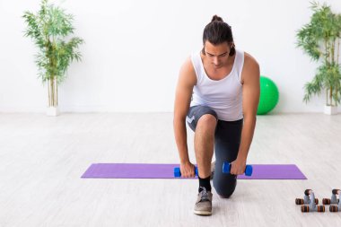 Genç yakışıklı adam içeride spor yapıyor.