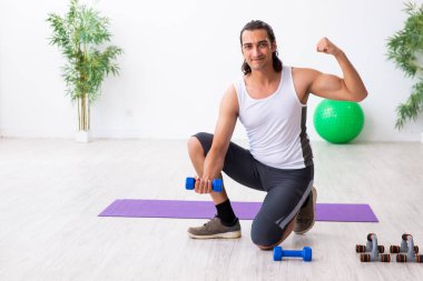 Genç yakışıklı adam içeride spor yapıyor.