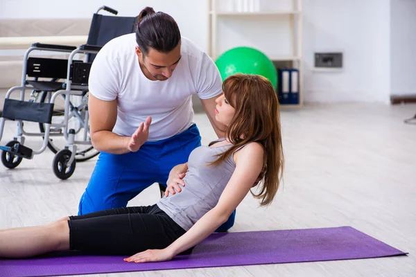 Mężczyzna fizjoterapeuta robi ćwiczenia z ranną kobietą na podłodze — Zdjęcie stockowe