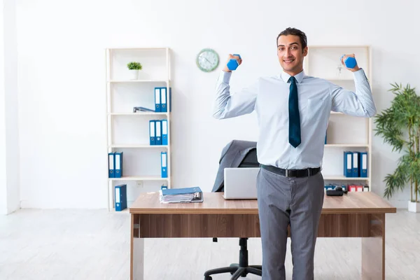 Jovem e bonito funcionário fazendo exercícios esportivos no local de trabalho — Fotografia de Stock