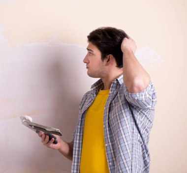 Evdeki duvara alçı yapıştıran genç adam.