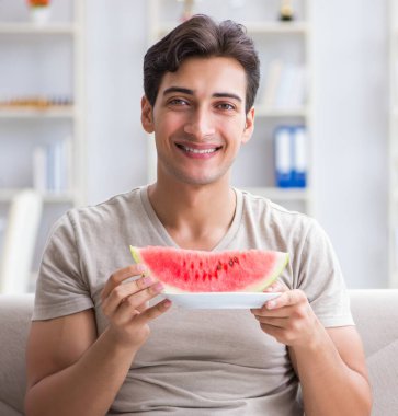 Evde karpuz yiyen bir adam.