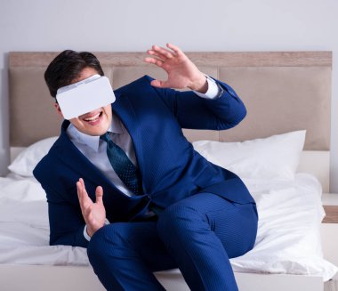 Yatak odasında sanal gerçeklik kulaklığı takan bir iş adamı.