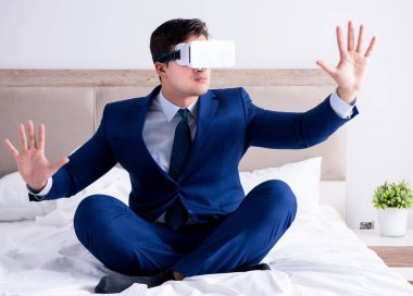 Yatak odasında sanal gerçeklik kulaklığı takan bir iş adamı.