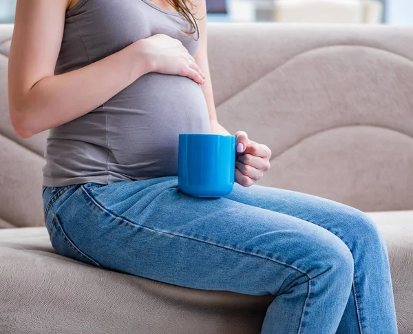 Femeie gravidă cu burtă stând pe o canapea acasă — Fotografie, imagine de stoc