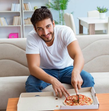 Pizza yiyen adam evde yemek yiyor, dinleniyor.