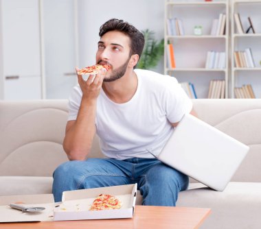 Pizza yiyen adam evde yemek yiyor, dinleniyor.