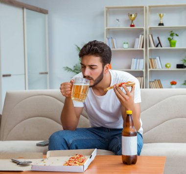 Pizza yiyen adam evde yemek yiyor, dinleniyor.