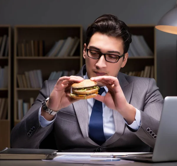 Affärsman sent på kvällen äter en hamburgare — Stockfoto