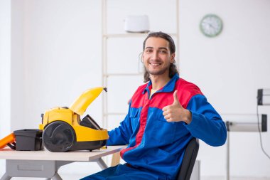 Genç erkek müteahhit atölyede elektrik süpürgesi tamir ediyor.