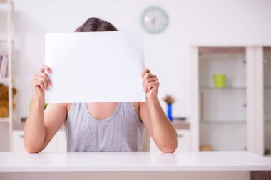 Evinde boş kağıt tutan genç bir adam.