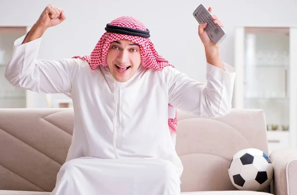 Młody arabski człowiek oglądając piłkę nożną siedzi na kanapie — Zdjęcie stockowe